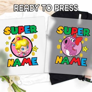 May include: Two iron-on transfers for t-shirts featuring a pink and purple character with a crown and a pink character with a bow. The text "SUPER NAME" is in rainbow colors.