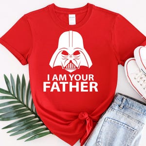 May include: Red t-shirt with a white graphic of Darth Vader's helmet and the text "I am your father".