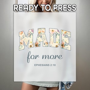 Op de afbeelding: Een wit T-shirt met een bloemenontwerp met de tekst "MADE for more EPHESIANS 2:10".