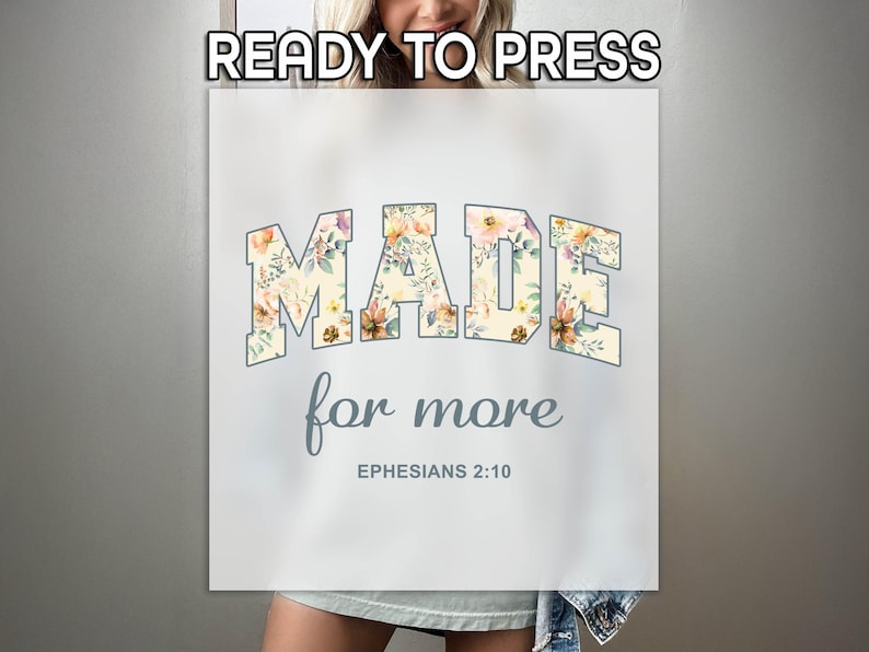 Op de afbeelding: Een wit T-shirt met een bloemenontwerp met de tekst "MADE for more EPHESIANS 2:10".