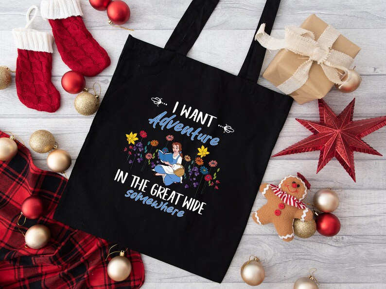 May include: Black tote bag with the text "I WANT Adventure IN THE GREAT WIDE somewhere". The bag features a colorful illustration of a woman reading a book surrounded by flowers. Christmas decorations are in the background.