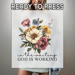 May include: A white t-shirt with a floral design and the text "in the waiting GOD IS WORKING".