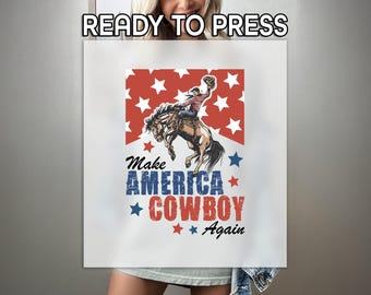 May include: A white t-shirt with a red, white, and blue graphic of a cowboy riding a bucking horse. The graphic includes stars and the text "Make America Cowboy Again".