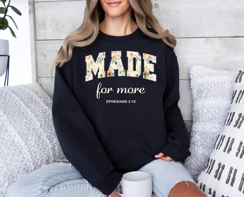 Op de afbeelding: Zwart sweatshirt met bloemenlettertype met de tekst "MADE for more" en de Bijbeltekst Efezi&euml;rs 2:10.