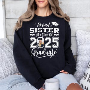 May include: Black sweatshirt with white text that reads "Proud Sister of a Class of 2025 Graduate". A photo of a graduate is in the center of the text.