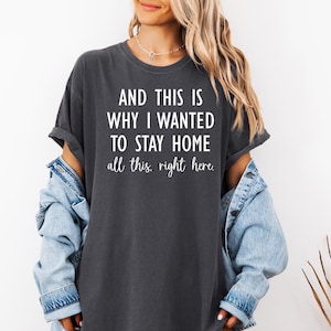 May include: Dark gray t-shirt with the text "AND THIS IS WHY I WANTED TO STAY HOME all this, right here." The shirt has rolled-up sleeves and a relaxed fit. A denim jacket is worn over the shirt.