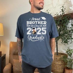 May include: A navy blue t-shirt with white text that reads "Proud Brother Of a Class Of 2025 Graduate". A photo of a person wearing a graduation cap is in the center of the shirt.