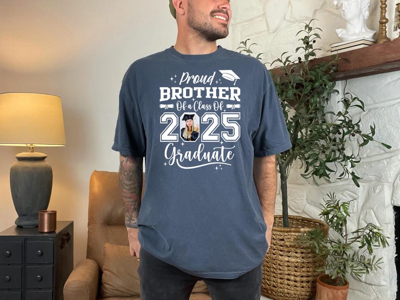 May include: A navy blue t-shirt with white text that reads "Proud Brother Of a Class Of 2025 Graduate". A photo of a person wearing a graduation cap is in the center of the shirt.