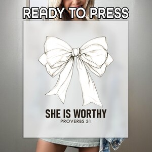 May include: A white t-shirt with a black and white illustration of a bow. The text "She is Worthy Proverbs 31" is printed below the bow.