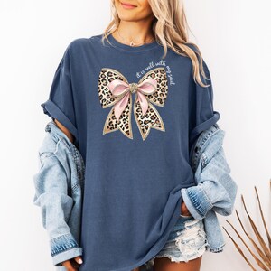 May include: A navy blue t-shirt with a large pink and leopard print bow with gold glitter accents. The text "It is well with my soul" is written in white on the bow.