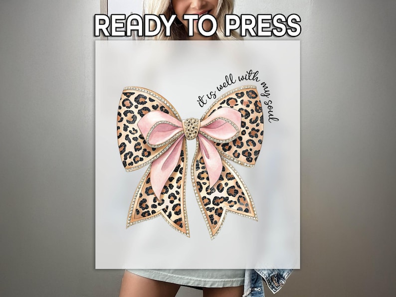 May include: A white t-shirt with a pink and brown leopard print bow with rhinestones and the text "It is well with my soul".