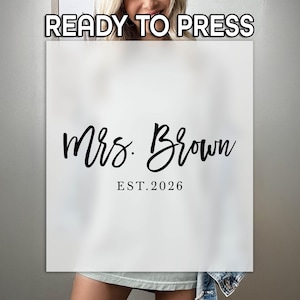 May include: A white square transfer sheet featuring the black text READY TO PRESS at the top, followed by the script text Mrs. Brown and the serif text EST. 2026 centered below. The design is presented on a semi-transparent overlay.