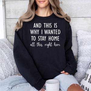 May include: Black sweatshirt with the text "AND THIS IS WHY I WANTED TO STAY HOME all this, right here." The text is in white, and the sweatshirt is worn by a person. The sweatshirt is a casual style.
