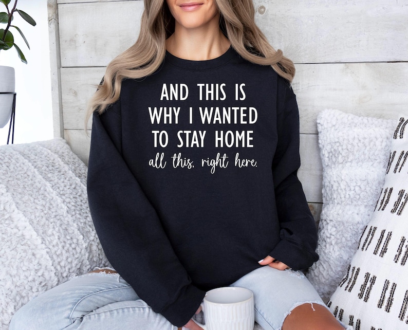 May include: Black sweatshirt with the text "AND THIS IS WHY I WANTED TO STAY HOME all this, right here." The text is in white, and the sweatshirt is worn by a person. The sweatshirt is a casual style.