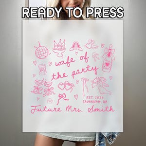 May include: White tote bag with pink illustrations and text. The bag features drawings of a disco ball, crown, champagne bottle, and other wedding-themed icons. Text includes "wife of the party," "Future Mrs. Smith," and "EST. 2026 Savannah, GA."