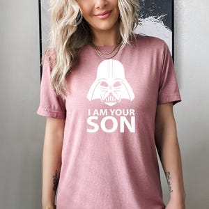 May include: A pink t-shirt with a white graphic of Darth Vader's helmet and the text "I am your son".