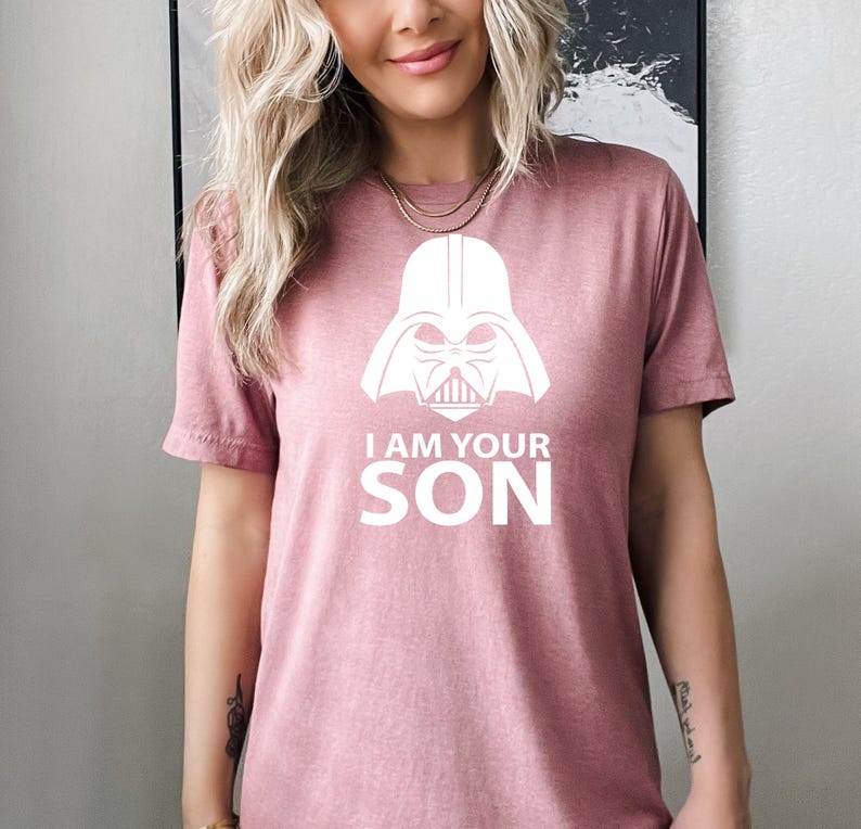 May include: A pink t-shirt with a white graphic of Darth Vader's helmet and the text "I am your son".