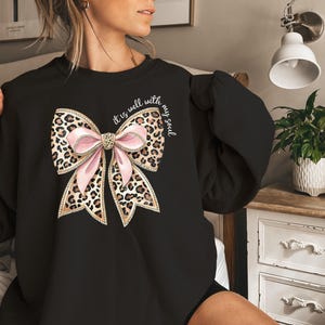 May include: Black sweatshirt with a pink and brown leopard print bow and the text "It is well with my soul".