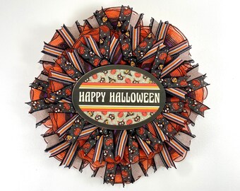 May include: A Halloween wreath featuring orange, black and white ribbon. The wreath has a sign that reads "Happy Halloween".