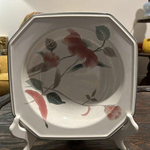 May include: A white octagonal ceramic bowl with a floral design. The bowl features pink and green flowers and leaves on a white background. The bowl has a dark green rim.