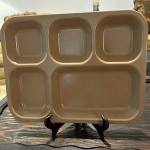 Puede incluir: Una bandeja de metal marrón con cinco compartimentos. La bandeja está sobre un soporte de madera.