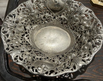May include: A silver decorative bowl with an intricate floral design. The bowl is made of metal and has a round shape. It is perfect for serving fruit or other small items.