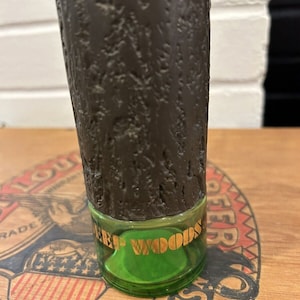 May include: A brown glass bottle with a textured surface and a green glass cap. The cap has a gold label that reads "Deep Woods".