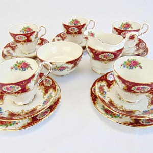 May include: A classic tea set with white teacups, saucers, and a creamer, adorned with a burgundy border and floral pattern. The set comprises six teacups, saucers, and a creamer, all with gold detailing. A small bowl is also included.