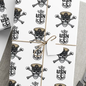 May include: White wrapping paper with a repeating pattern of a skull and crossbones with the letters USN. The skull is wearing a sailor hat.