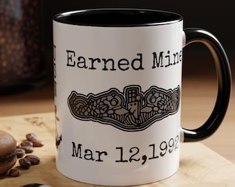 May include: A white ceramic mug with a black interior and handle. The mug features black text that reads Earned Mine and Mar 12, 1992, along with a black graphic illustration of a submarine warfare insignia centered between the two lines of text.