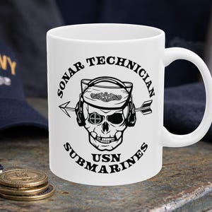 May include: White ceramic mug featuring a black and white skull design with the words "SONAR TECHNICIAN SUBMARINES USN". The skull wears a hat and has an arrow through it. The mug has a large handle.