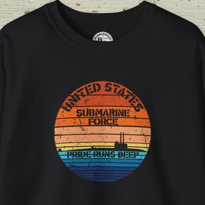 Puede incluir: Sudadera negra de cuello redondo con un gráfico circular. El gráfico presenta un diseño de puesta de sol con las palabras "United States Submarine Force" y "Pride Runs Deep". El diseño incluye una silueta de submarino.