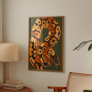 Puede incluir: Una impresión artística enmarcada que presenta una ilustración estilizada de una serpiente en tonos naranja, marrón y negro sobre un fondo verde oscuro. La serpiente está enroscada, con un patrón detallado. La obra de arte se exhibe en una habitación con una paleta de colores neutros.