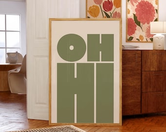 May include: A framed print with the word "OH HI" in large, bold, green letters on a white background. The print is hanging on a white wall above a wooden dresser.