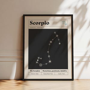 May include: A framed vertical poster featuring the Scorpio zodiac sign. The design includes the text Scorpio, October 23 - November 21, the Scorpio symbol, a white star constellation on a black background, and labels for element, planet, and quality.