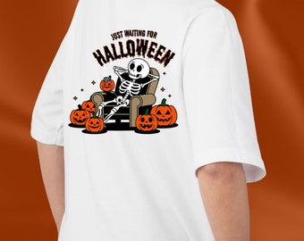 May include: White t-shirt with a skeleton sitting in a chair holding a pumpkin. The text "Just waiting for Halloween" is above the skeleton. There are pumpkins around the chair.