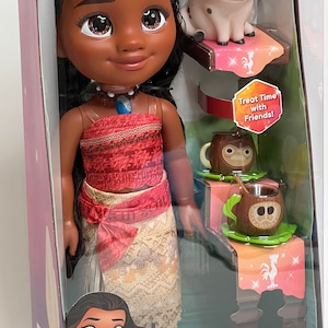 May include: A Disney Princess Moana doll set in a clear plastic package. The doll has dark hair, a red top, and a patterned skirt. The set includes a Pua pig figure and two coconut-shaped mugs. The packaging includes the text "Treat Time with Moana and Pua."
