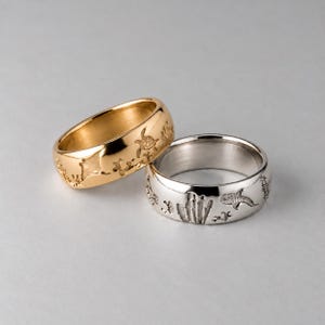 May include: Two metal rings, one gold-toned and one silver-toned, featuring engraved marine life designs including a sea turtle, a manta ray, a whale shark, and coral patterns on the outer surface of each band.
