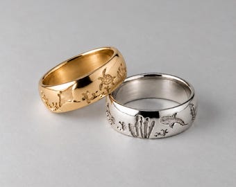 May include: Two metal rings, one gold-toned and one silver-toned, featuring engraved marine life designs including a sea turtle, a manta ray, a whale shark, and coral patterns on the outer surface of each band.