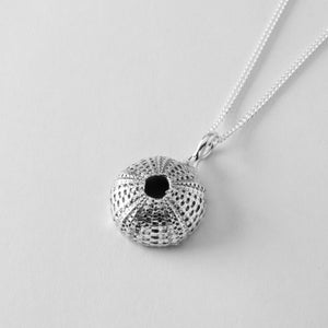 Puede incluir: Un collar de plata con un colgante de erizo de mar detallado. El colgante es una representación realista de una concha de erizo de mar.