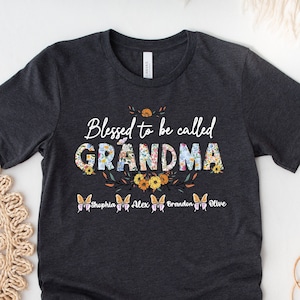 May include: A dark gray t-shirt with the text "Blessed to be called GRANDMA" in white with floral accents. The names "Sophia, Alex, Braeden, Olive" are printed in white below the text.