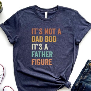 Pu&ograve; includere: Una maglietta blu scuro con il testo "It's not a dad bod it's a father figure" in un font retr&ograve; con accenti colorati.