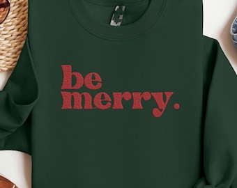 May include: A dark green sweatshirt with the words "be merry" in red lettering. The sweatshirt is laid flat on a white surface.
