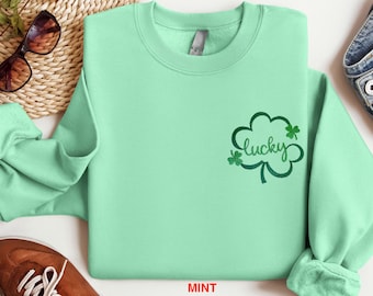 Könnte beinhalten: Ein mintgrüner Pullover mit einem grünen vierblättrigen Kleeblatt-Motiv und dem Wort "lucky" im Kleeblatt.