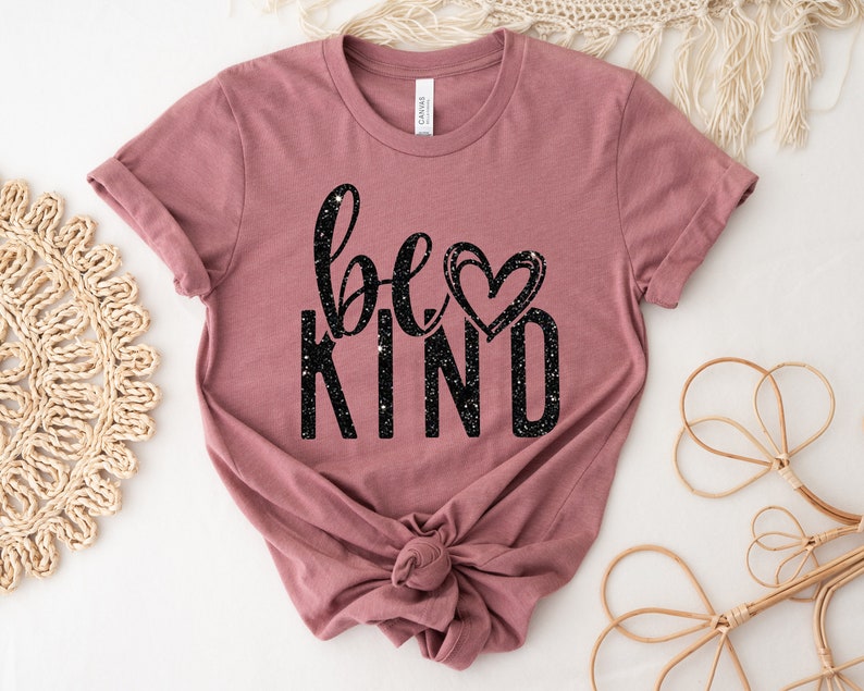 May include: A mauve t-shirt with the text "be kind" in black glitter lettering and a small heart graphic.