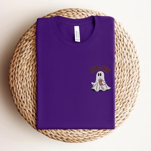 May include: Purple t-shirt with a white ghost holding a brown beverage and the text "BOO-JEE" in black.