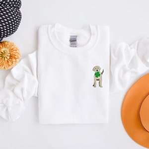 May include: White sweatshirt with a light brown dog embroidered on the front holding a green shamrock.