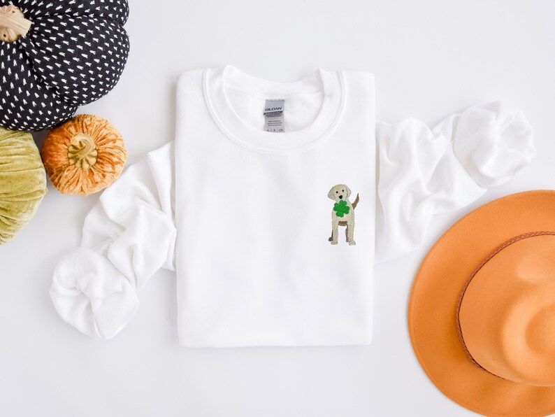 May include: White sweatshirt with a light brown dog embroidered on the front holding a green shamrock.
