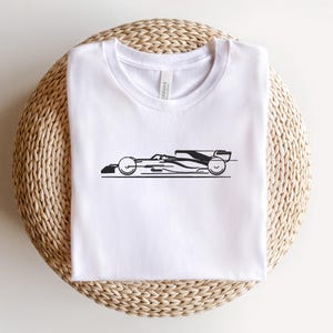 May include: White t-shirt with a black silhouette of a racing car on the front.