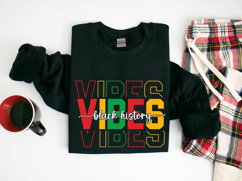 May include: Black sweatshirt with the text "VIBES black history VIBES" in red, green, and yellow lettering. The sweatshirt is folded and laid flat on a white surface.